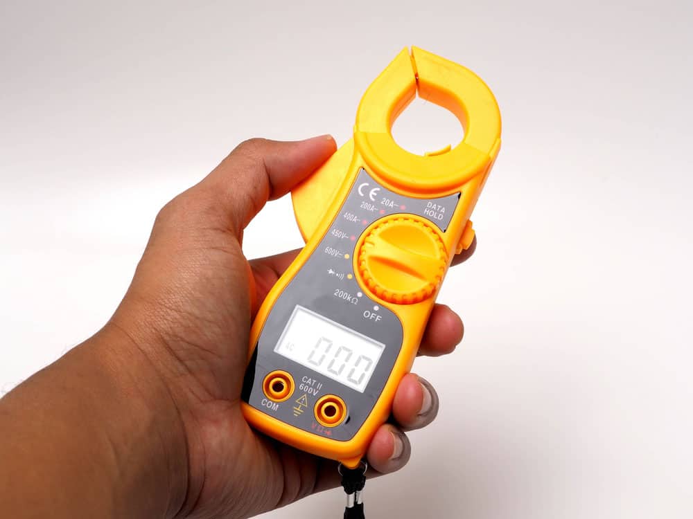A person using a yellow digital clamp meter